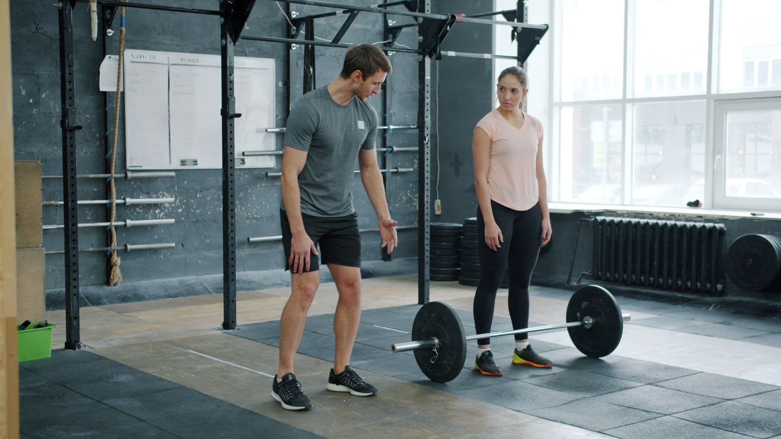 A coach explaining deadlift technique to a client in the gym