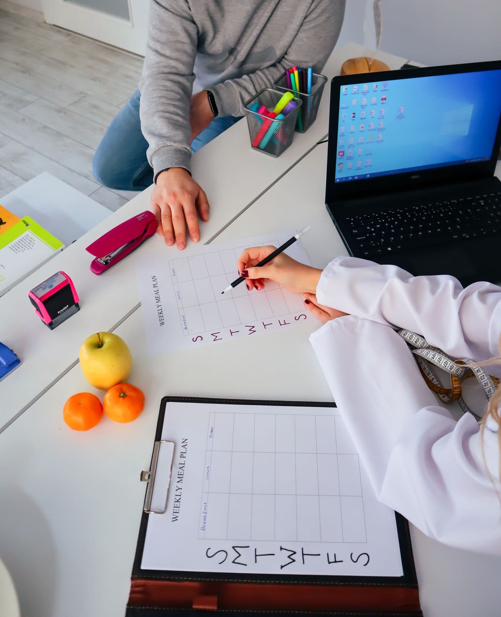 A nutritionist filling in a weekly meal plan with a client at a desk