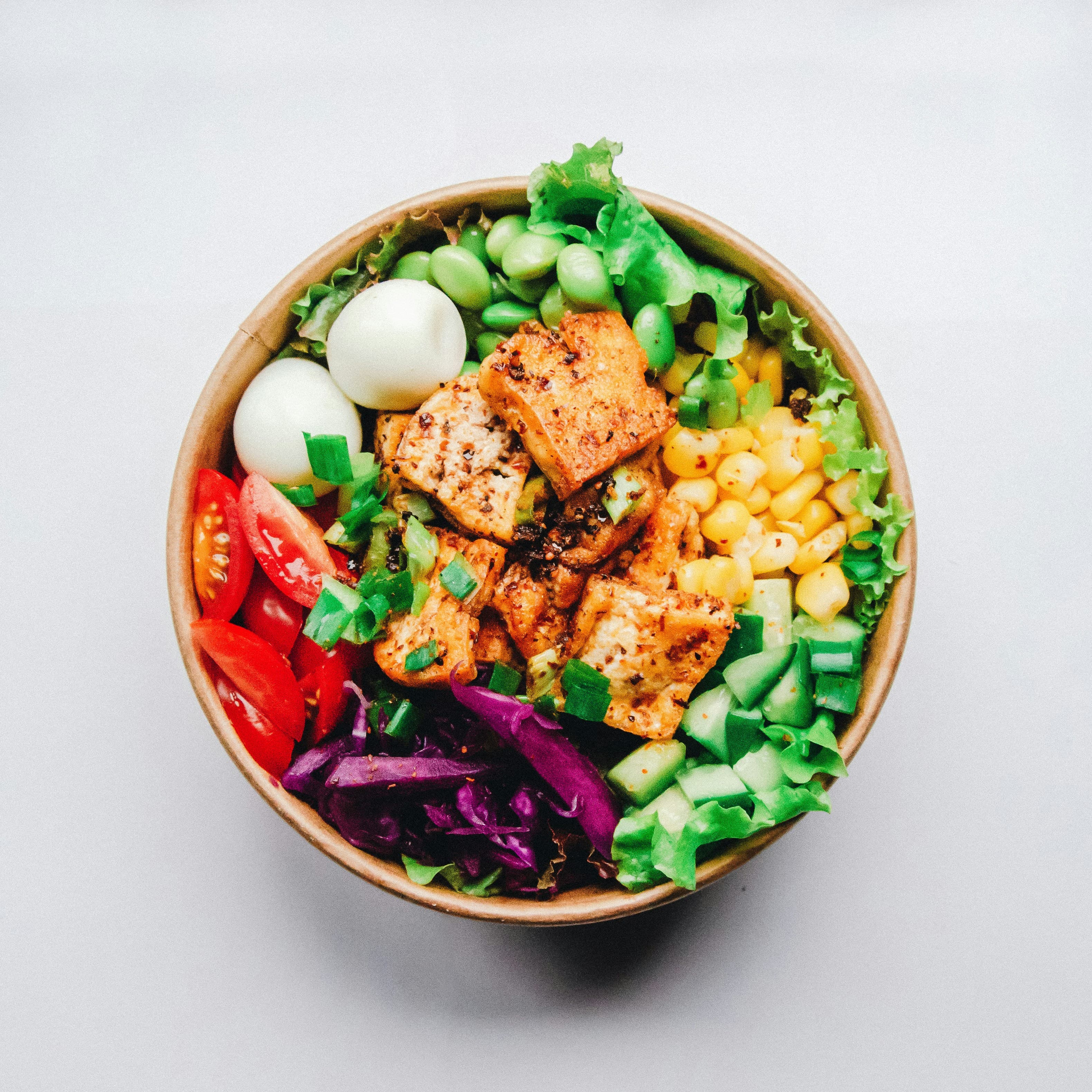 A bowl of salad with grilled tofu, egg, tomatoes and greens